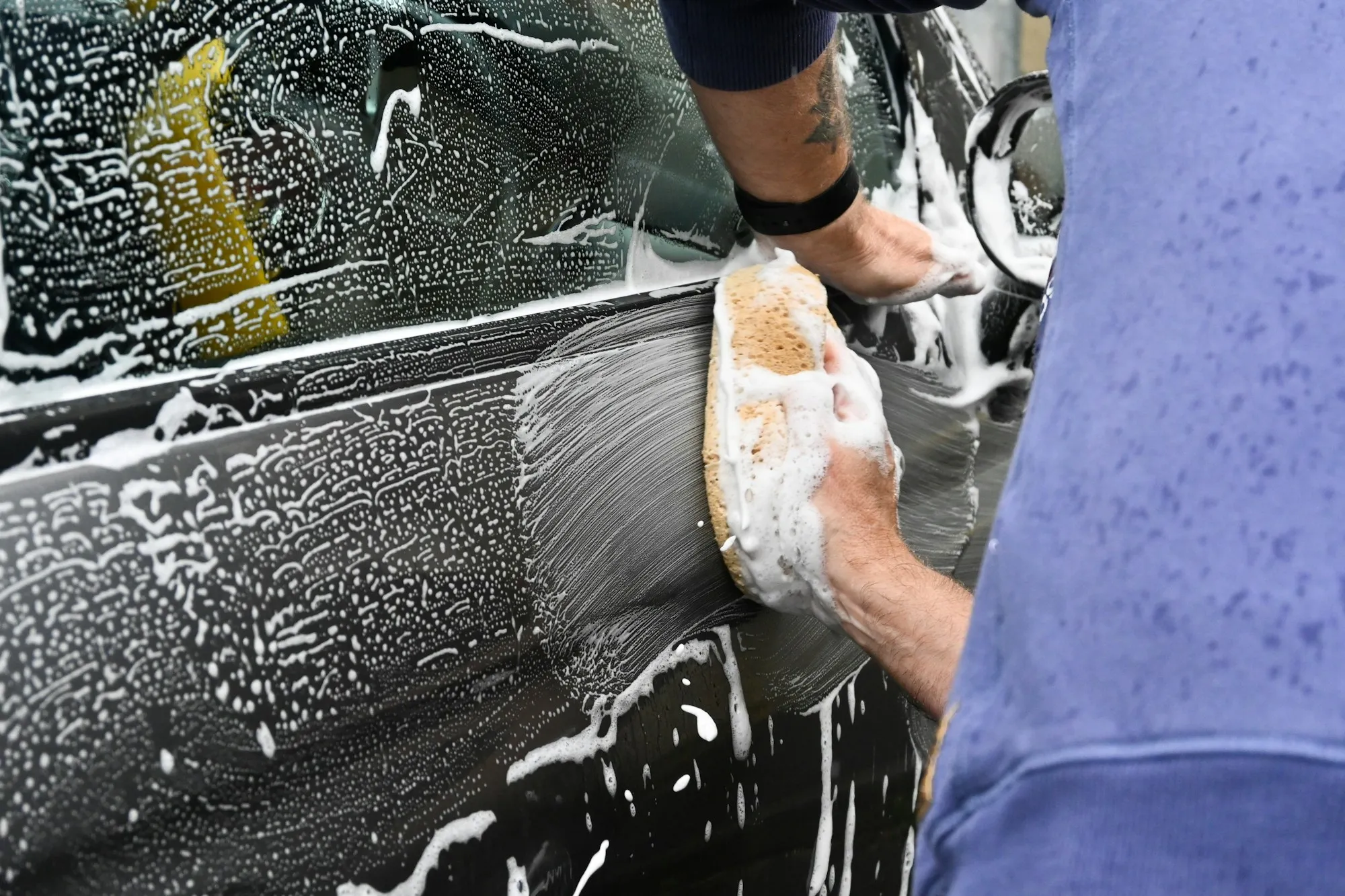 Hand washing a car with a soapy wash mitt